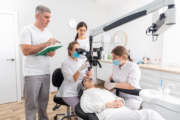 Group of young doctors learning in dental clinic watching dental treatment with microscope