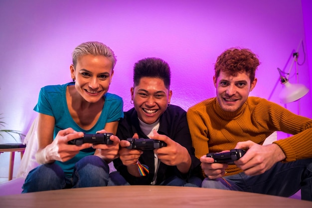 Group of young friends playing video games together on the sofa at home purple led competing looking at camera