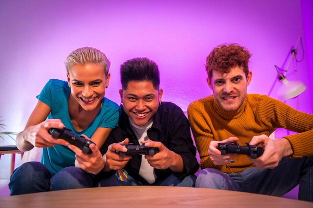 Group of young friends playing video games together on the sofa at home purple led young millennials