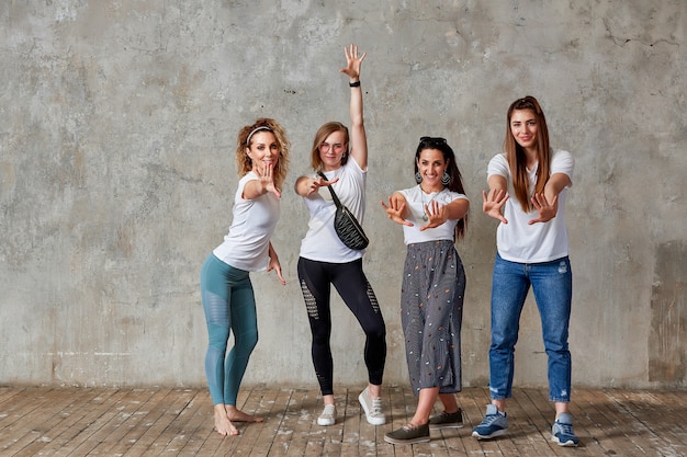 Group of young girls are posing against the wall smiling and showing gestures with their hands