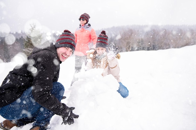 group of young happy business people having a competition in making snowmen while enjoying snowy winter day with snowflakes around them during a team building in the mountain forest