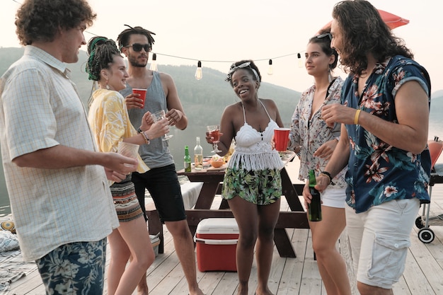 Group of young happy people dancing together and drinking alcohol during the party outdoors