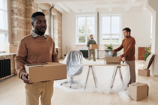 Group of young interracial employees carrying moving boxes in new office while setting up new space