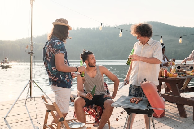 Group of young men drinking beer and talking to each other during the party on a pier