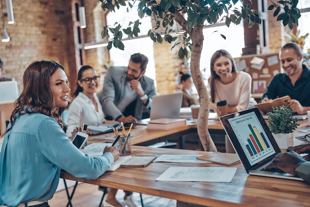 Group of young modern people in smart casual wear communicating and using modern technologies while working in the office