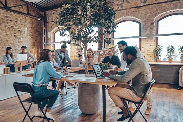 Group of young modern people in smart casual wear communicating and using modern technologies while working in the office