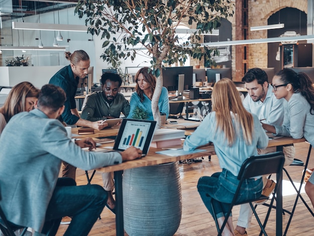 Group of young modern people in smart casual wear communicating and using modern technologies while working in the office