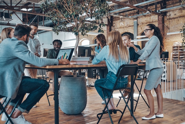 Group of young modern people in smart casual wear communicating and using modern technologies while working in the office