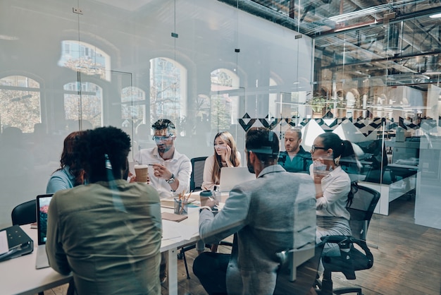 Group of young modern people in smart casual wear discussing business while working in the board room