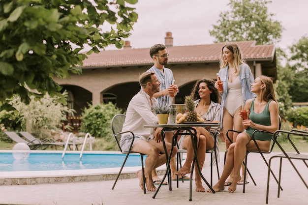 Group of young people cheering with cider by the pool in the garden