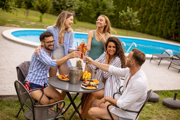 Group of young people cheering with cider by the pool in the garden