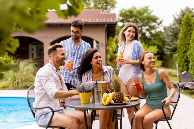 Group of young people cheering with cider by the pool in the garden