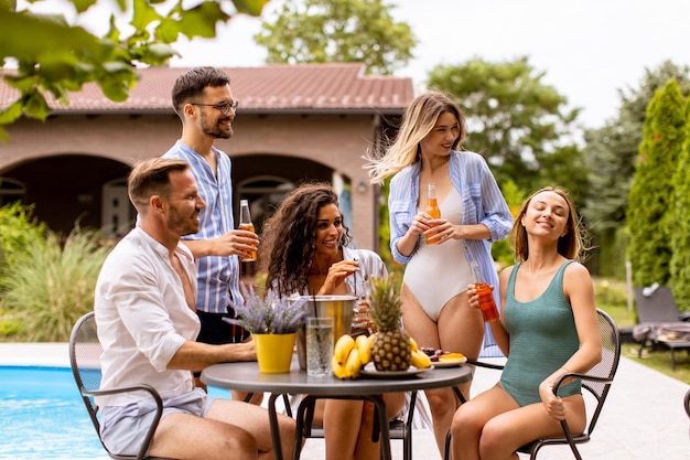 Group of young people cheering with cider by the pool in the garden