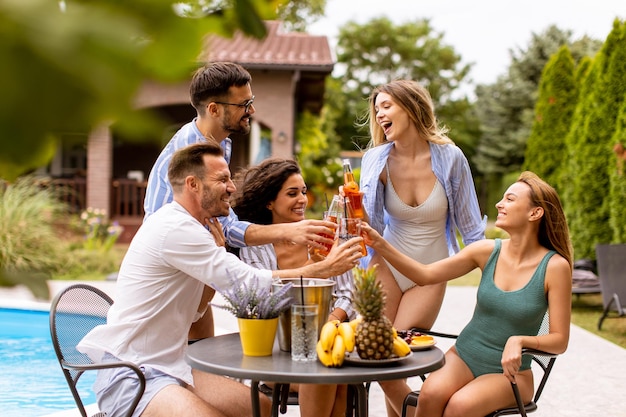 Group of young people cheering with cider by the pool in the garden