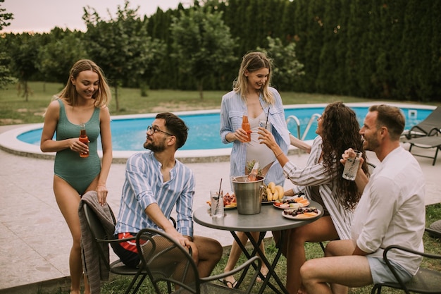 Group of young people cheering with cider by the pool in the garden