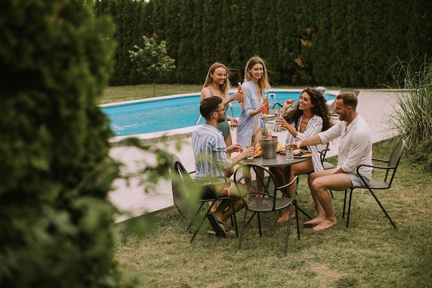 Group of young people cheering with cider by the pool in the garden