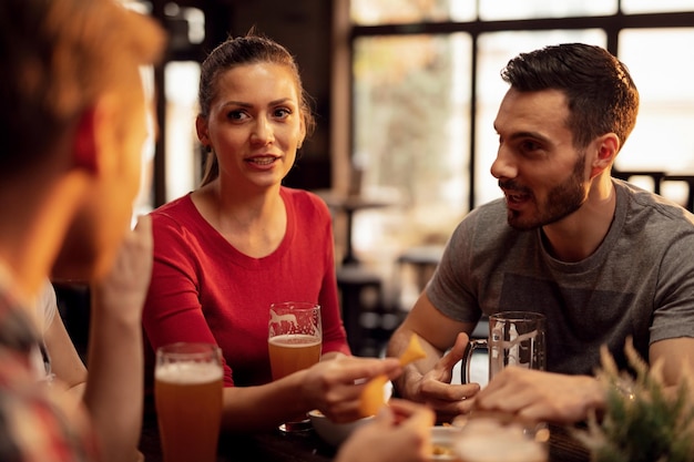 Group of young people drinking beer and eating tortilla chips while spending time together in a tavern Focus is on young woman