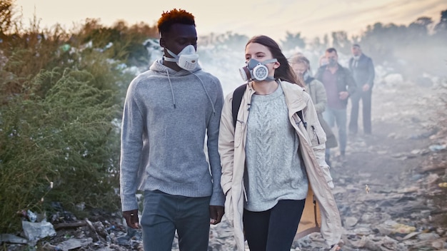 Group of young people in gas masks going through the toxic smoke in a garbage dump people care about...