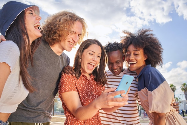 Group of young people having fun watching something on their cell phones the boys hug and laugh with