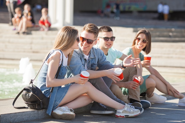 Group of young people near the fountain drinking coffee and having fun. friends relaxing outdoors.