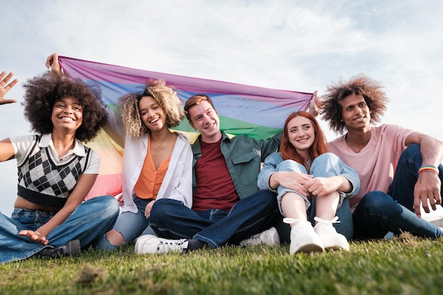 Group of young people sitting on the grass with the gay pride flag Concept friendship lgtbi symbols