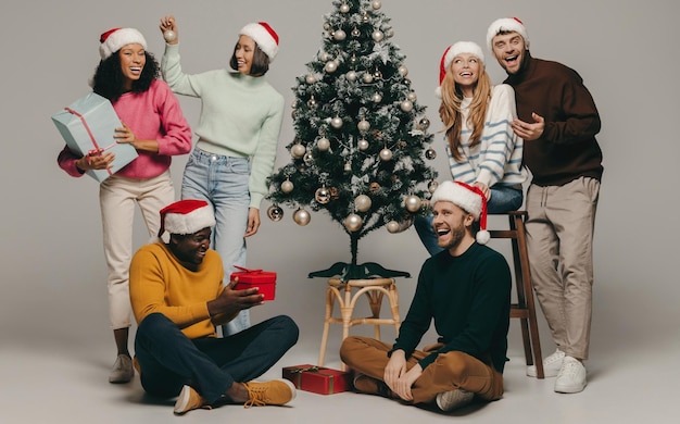 Group of young people smiling while having fun near the Christmas tree on studio background