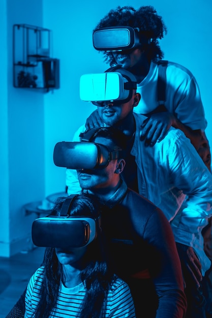 Group of young people with vr glasses in a virtual reality game in a blue light in formation on top of each other futuristic or science technology concept