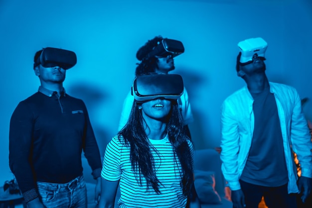 Group of young people with vr glasses in a virtual reality game in a blue light futuristic or science technology concept amazed by the realism