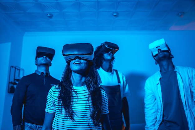 Group of young people with vr glasses in a virtual reality game in a blue light futuristic or science technology concept playing together at home