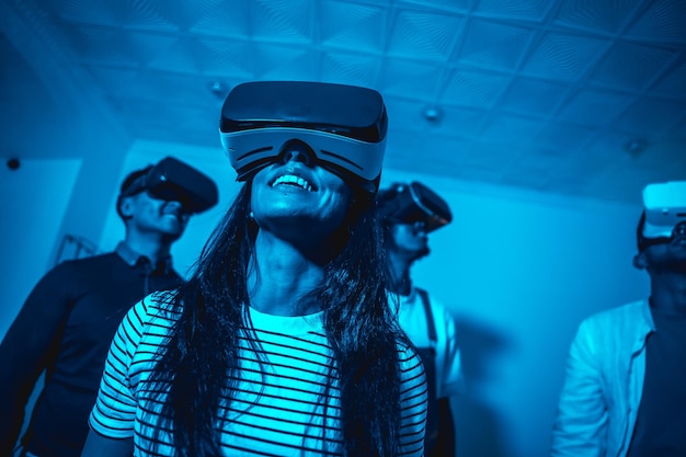 Group of young people with vr glasses in a virtual reality game in a blue light futuristic or science technology concept playing together at home