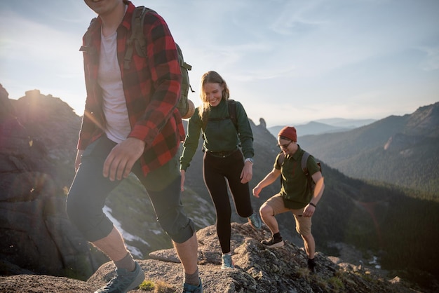 Group of young tourists two guys and girl with backpacks in mountains go along route