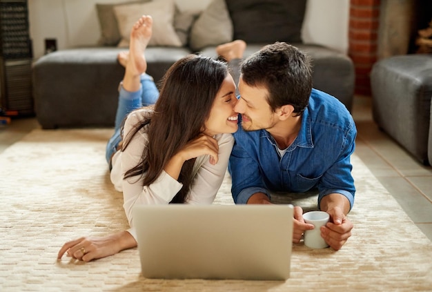 Growing closer by the day Shot of an affectionate young couple lying down on the carpet and using their laptop at home