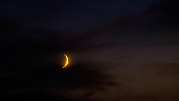 Growing moon in dark cloudy evening sky Dark colors of summer night