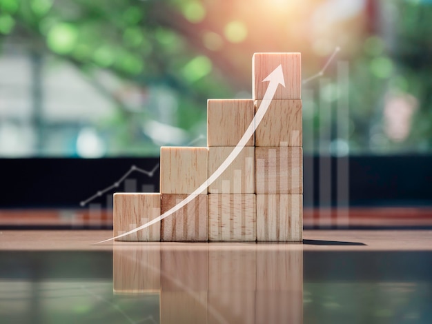 Growth chart and graph. Glowing rise up arrow on the top of wooden blocks chart steps on wooden desk with copy space, eco style. The business growth process, finance, and economic improvement concept.