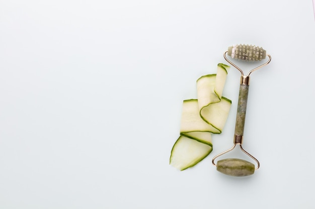 Gua Sha facial massage tools and cucumber. Quartz jade roller on pastel background. Anti age, lifting and toning treatment at home.