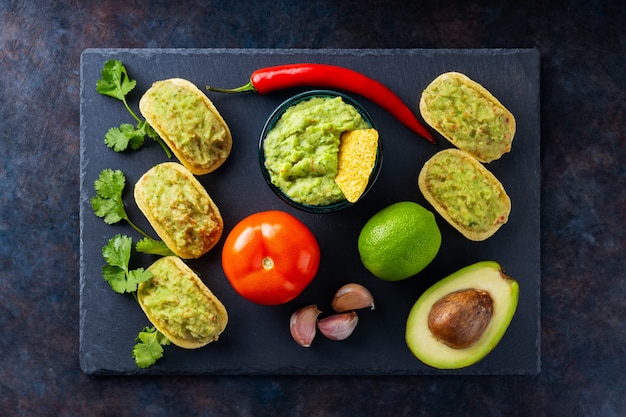 Guacamole sauce, nachos chips and ingredients on a dark background