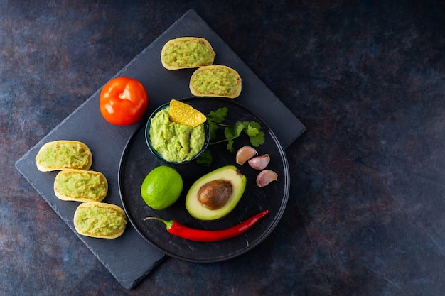 Guacamole sauce, nachos chips and ingredients on a dark background