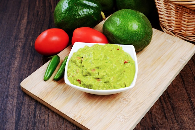 Guacamole served on a white plate on a wooden table. Guacamole ingredients.