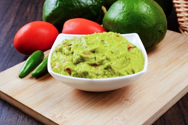 Guacamole served on a white plate on a wooden table. Guacamole ingredients.