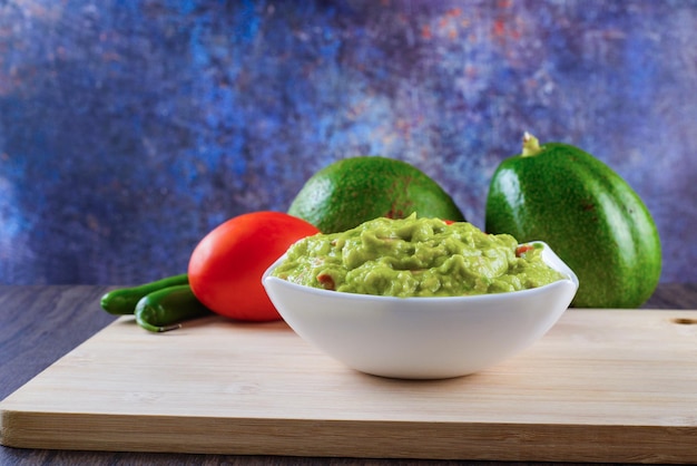 Guacamole served on a white plate on a wooden table. Guacamole ingredients.