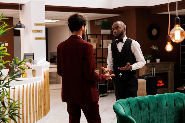 Photo guest and bellboy discussing in lobby, asking about local recommendations while he is visiting on business trip. white collar worker being greeted by bellhop at hotel, luxury services.