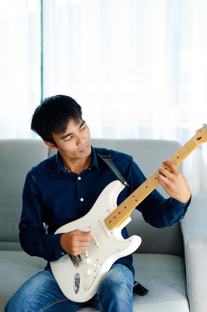 Guitarist playing guitar on sofa at home Practicing guitar at home Relax by playing stringed instruments