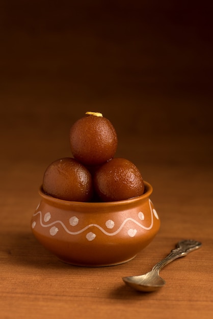 Gulab Jamun in clay pot with spoon and dry fruits. Indian Dessert or Sweet Dish