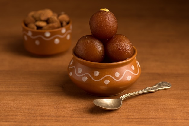 Gulab Jamun in clay pot with spoon and dry fruits. Indian Dessert or Sweet Dish