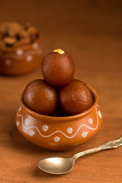 Gulab Jamun in clay pot with spoon and dry fruits. Indian Dessert or Sweet Dish