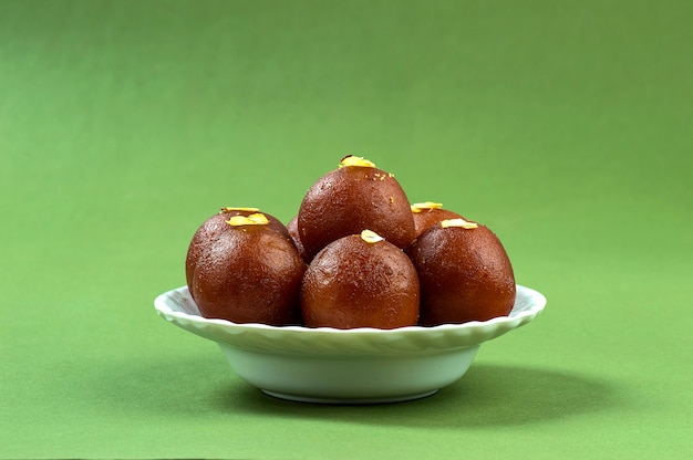 Gulab Jamun, Indian dessert topped with pistachio in white plate on green