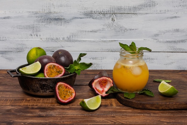 Gulupa or passion fruit juice surrounded by peels and whole and cut fruits lemons and spearmint on white wooden background