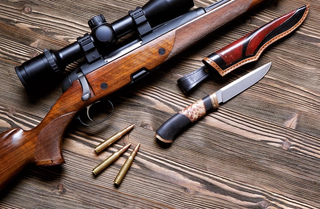 A gun with an optical sight a hunting knife on a wooden backgroundTop view