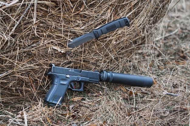 A gun with silencer and tactical knife is laying on a bale of hay