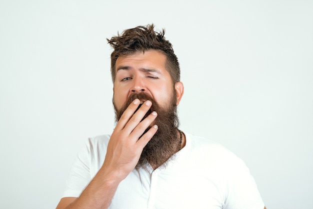 Guy awake with mouth opened in yawn, copy space. Morning and wake up, everyday life. Man with yawning sleepy face on white background. Hipster with beard with messy hair. Morning yawning concept.